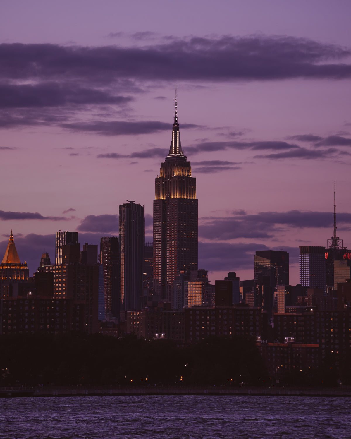 The Empire State Building above the New York skyline from across the East River, lit up in a purple sky just after sunset