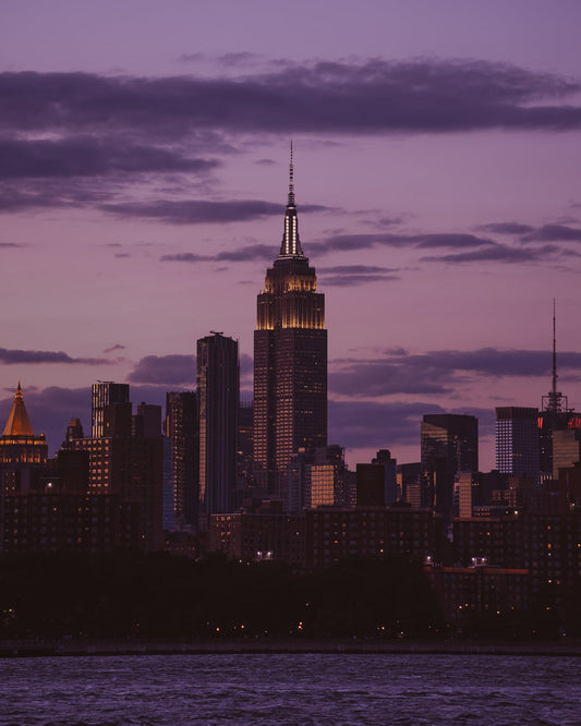 The Empire State Building above the New York skyline from across the East River, lit up in a purple sky just after sunset