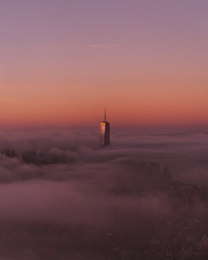 The top of the World Trade Center peeking out from thick fog over a pink sunrise
