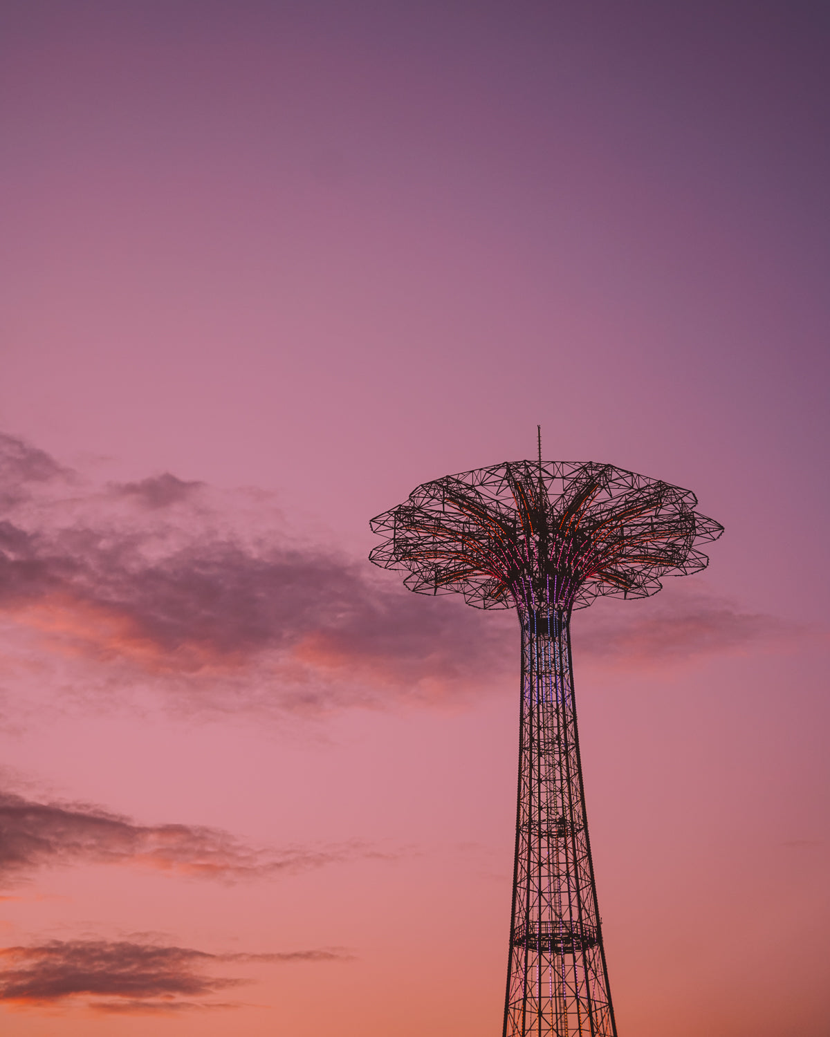 The iconic Coney Island parachute jump lit up against a bright pink and orange sunset