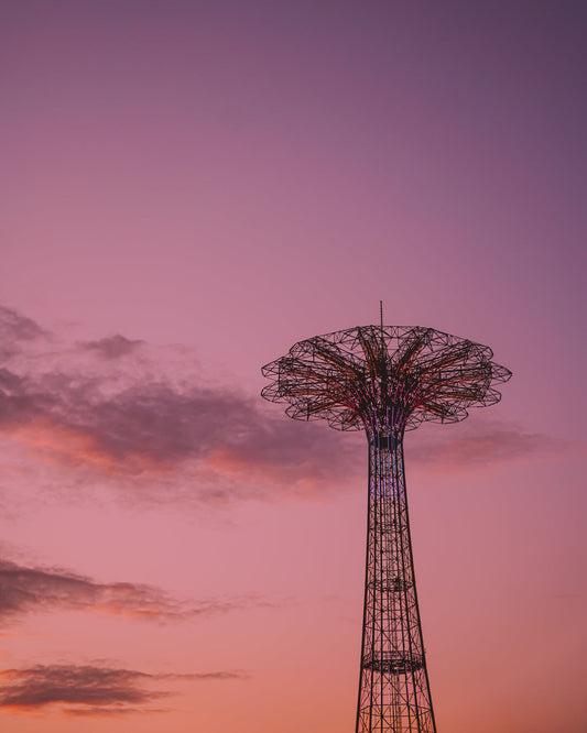 The iconic Coney Island parachute jump lit up against a bright pink and orange sunset