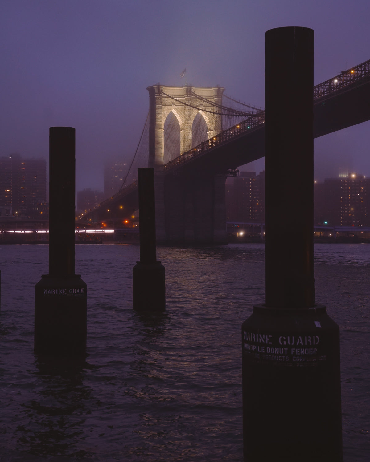 The Brooklyn Bridge lit up during a foggy blue hour sunset
