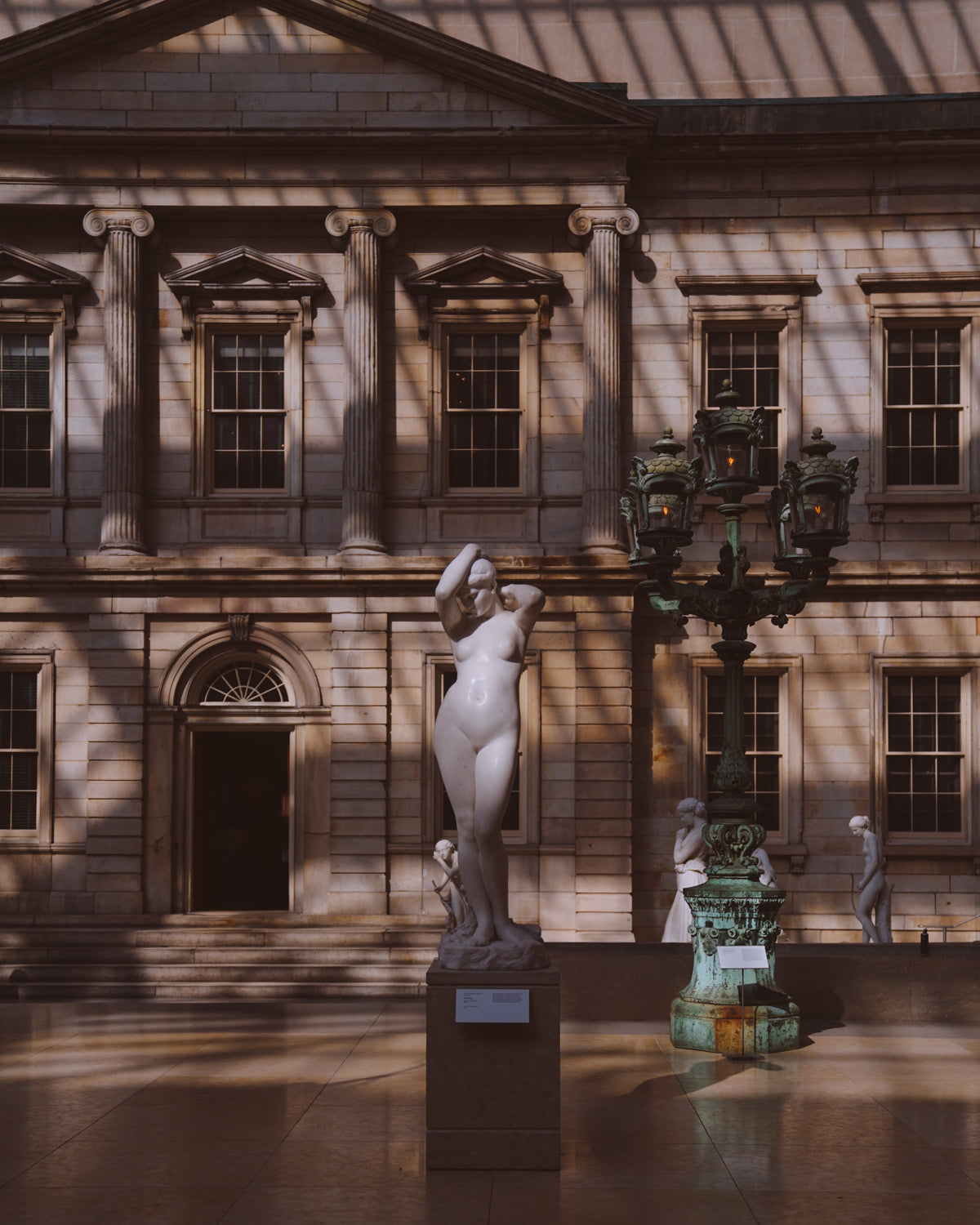 A marble statue of a woman in the center of a shadow filled room at The Met