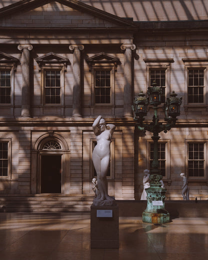 A marble statue of a woman in the center of a shadow filled room at The Met