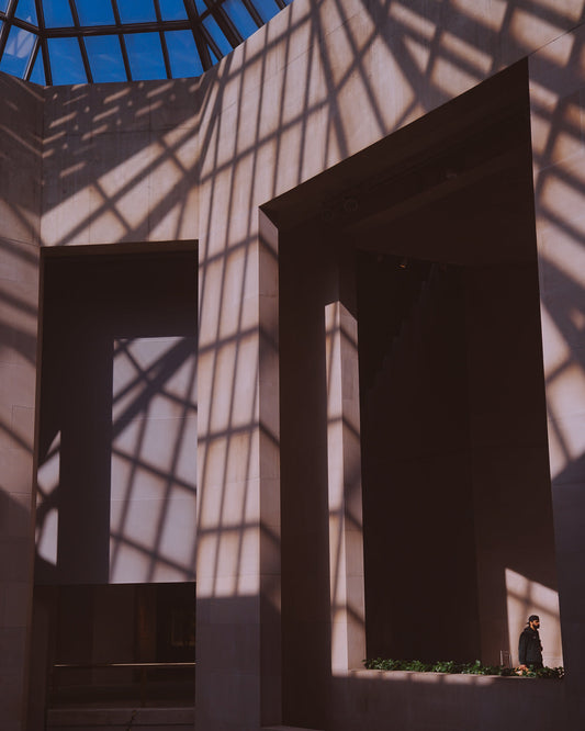 Harsh shadows layered over a round staircase at The Met with one person walking by in a patch of light