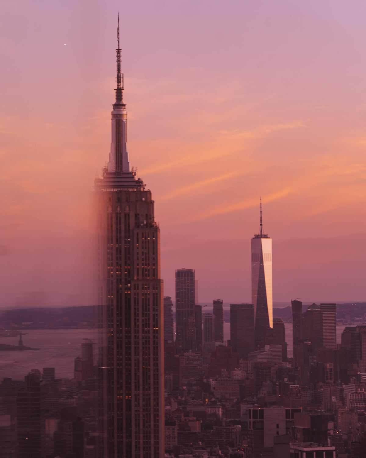 The Empire State Building against a pink and orange sunset, and half the building appears to be missing because it's behind a glass reflection