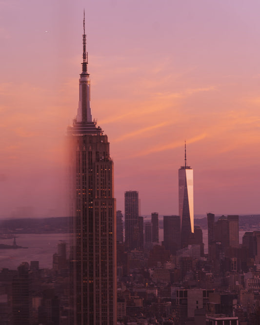 The Empire State Building against a pink and orange sunset, and half the building appears to be missing because it's behind a glass reflection