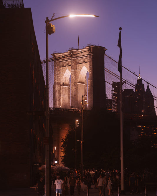 The Brookyn Bridge lit up at night with a street lamp appearing over the top of it also lit up