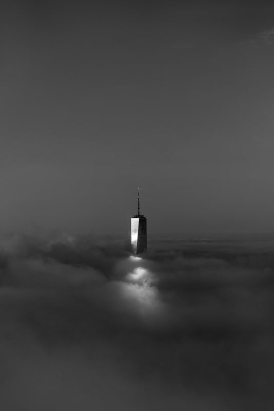 The top of the World Trade Center tower peeking out from dense fog across New York City during sunrise