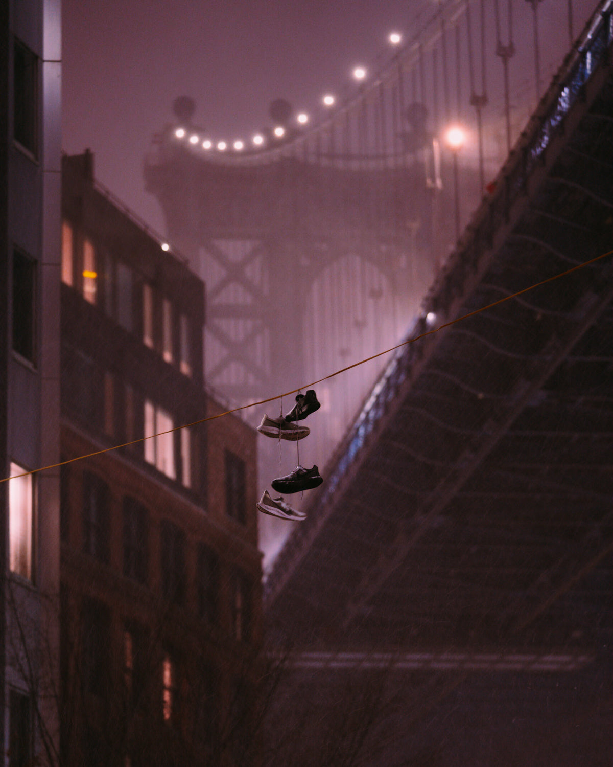 Two shoes handing from a wire in front of a blurry Manhattan Bridge during a snow storm