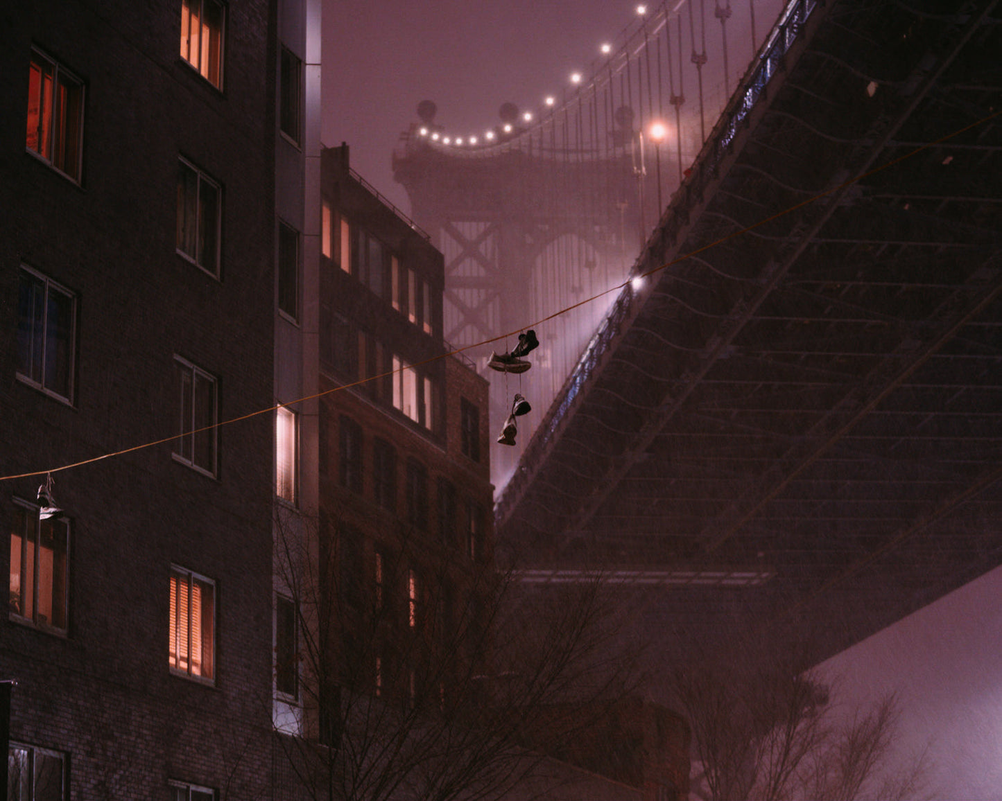 Two shoes handing from a wire in front of a blurry Manhattan Bridge during a snow storm