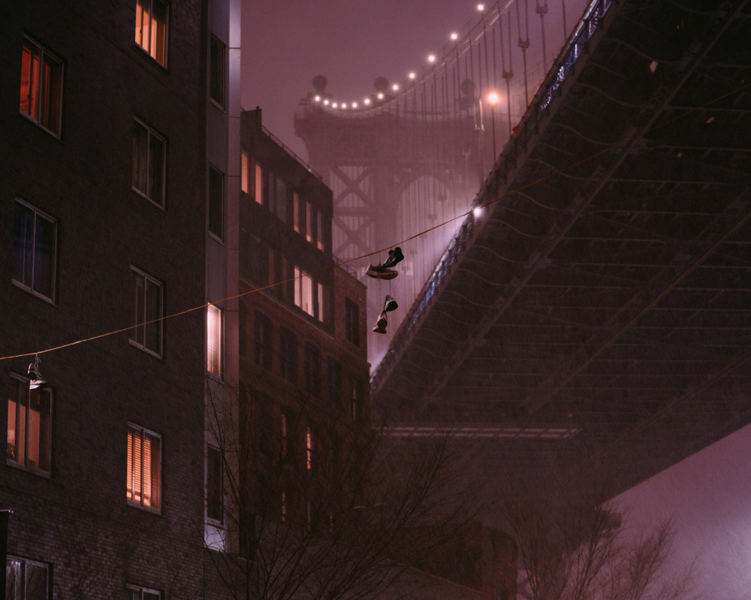 Two shoes handing from a wire in front of a blurry Manhattan Bridge during a snow storm