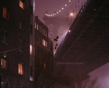 Two shoes handing from a wire in front of a blurry Manhattan Bridge during a snow storm